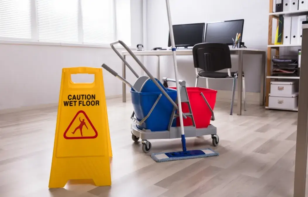 A cleaning cart with a mop and bucket next to a "Caution Wet Floor" sign in a modern office.