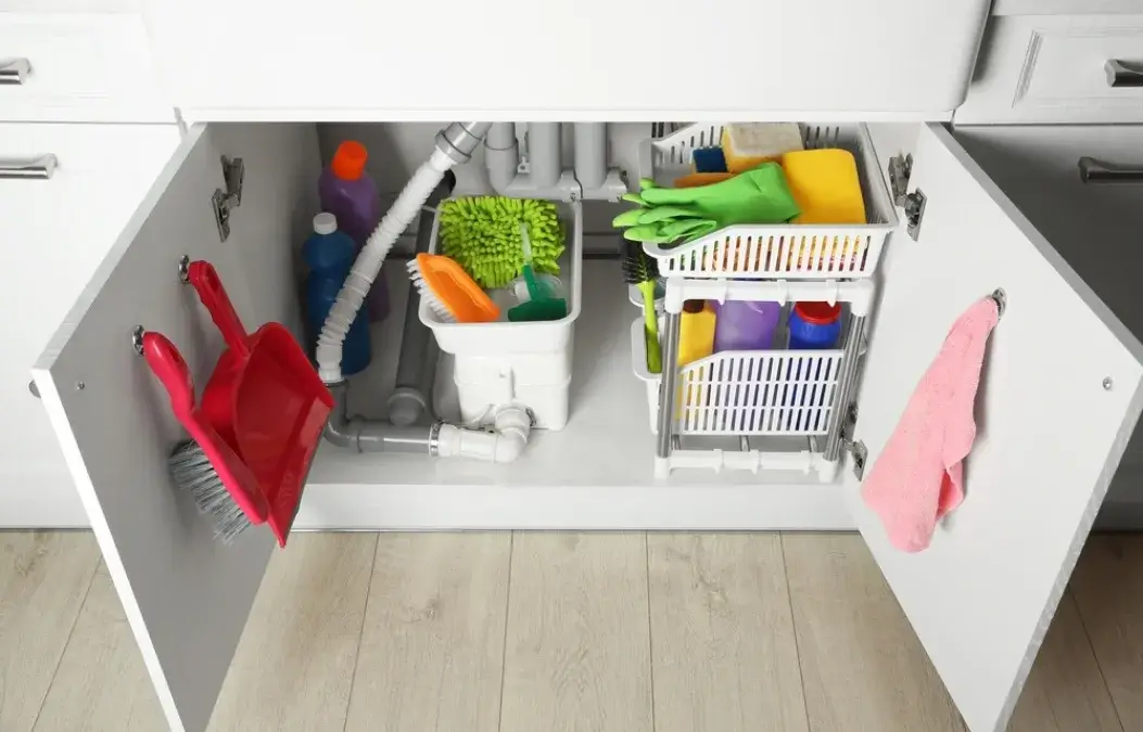 Organized cleaning supplies stored under a kitchen sink in white cabinets.