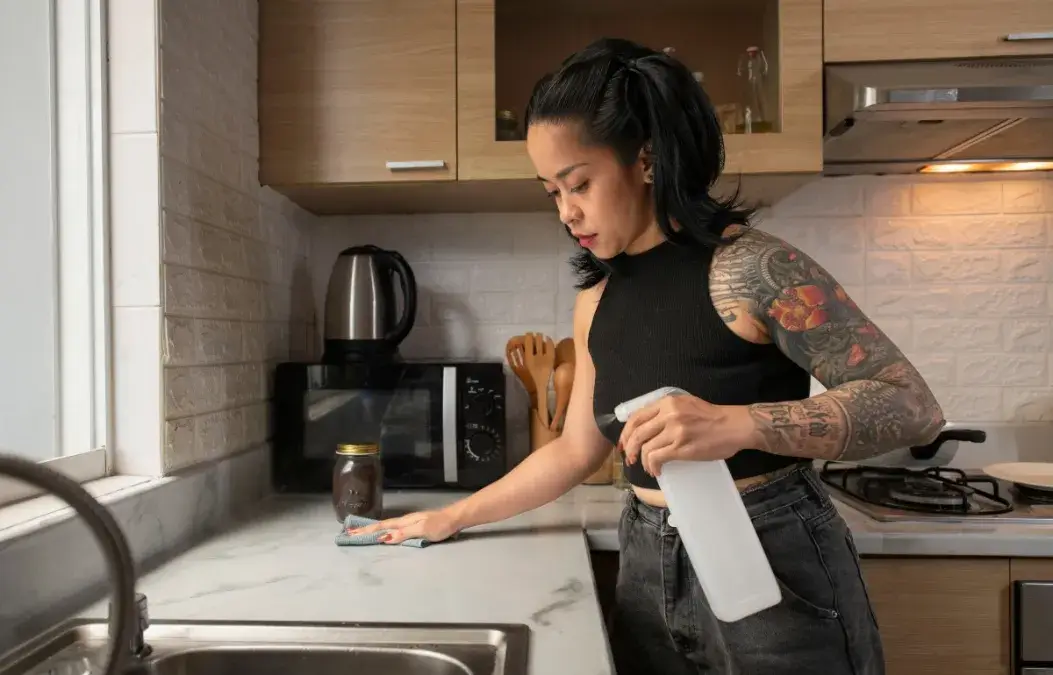 Woman cleaning a kitchen countertop with a spray bottle and cloth.