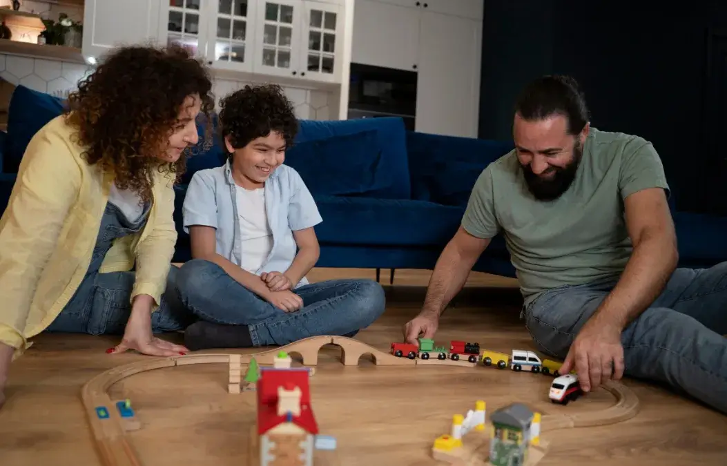 A happy family playing with a wooden train set on the living room floor.