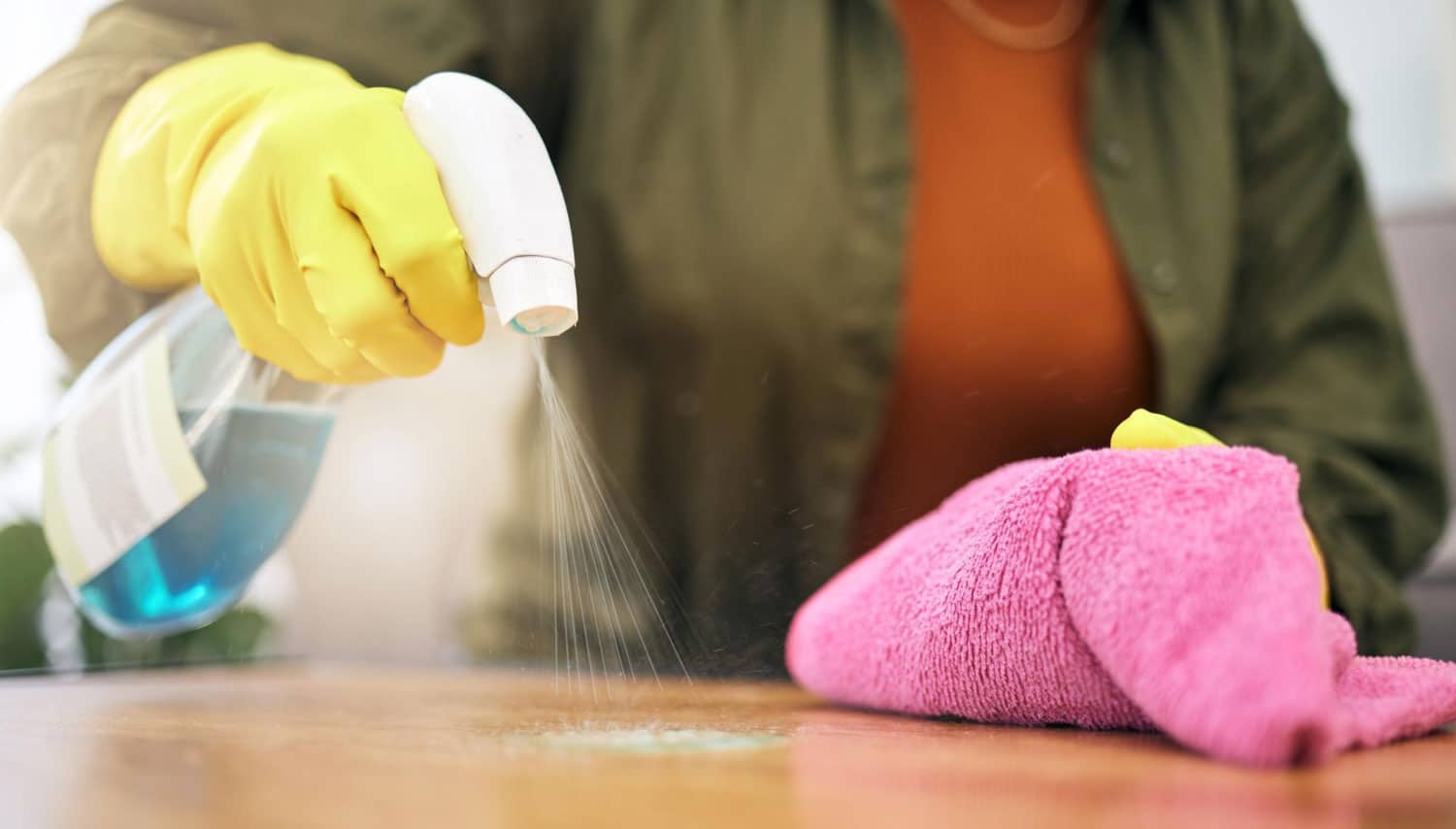 Person wiping a wooden table as part of a home cleaning checklist.
