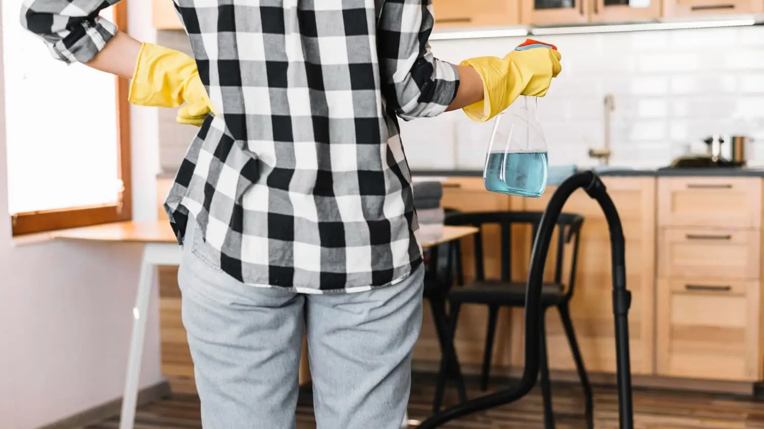 Woman in yellow gloves holding cleaning spray, ready for short-term rental cleaning.