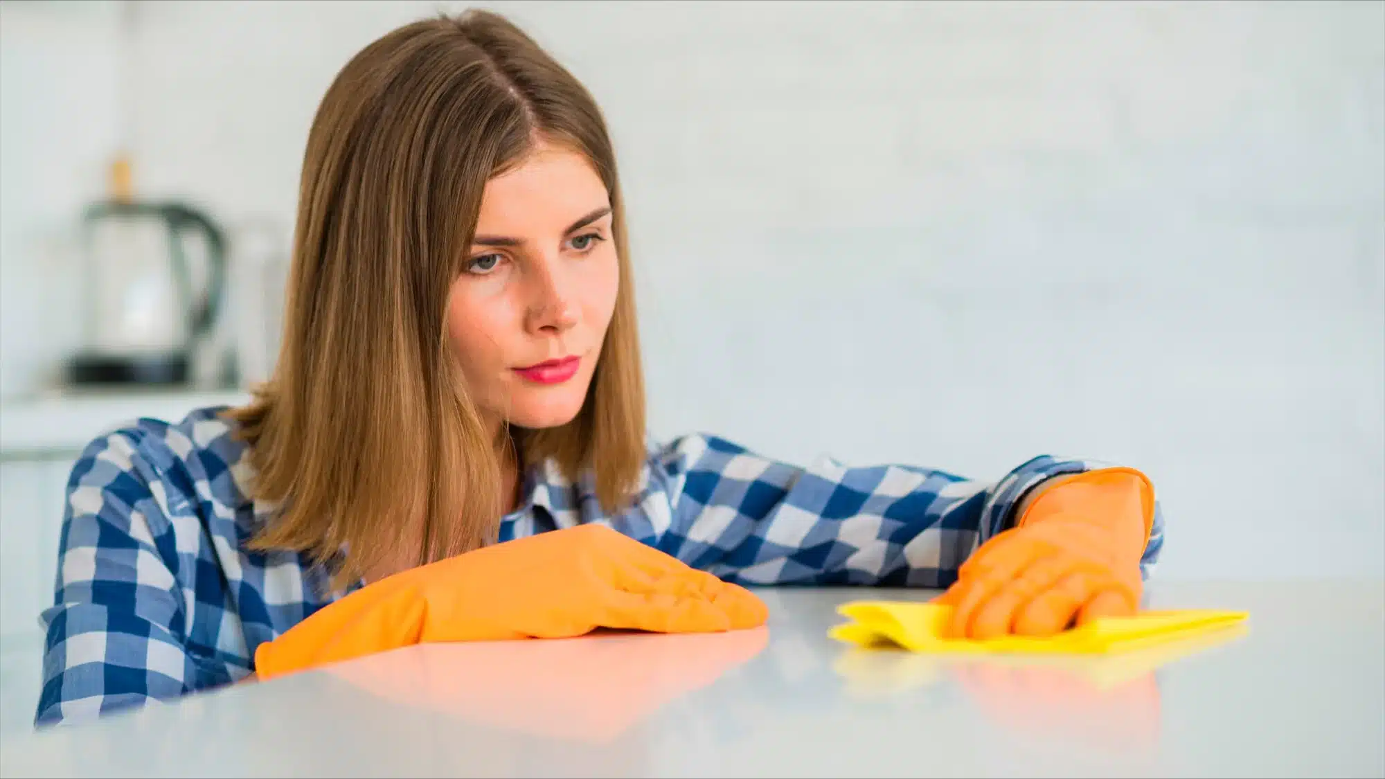 Woman in orange gloves wiping a kitchen counter with a yellow cloth.