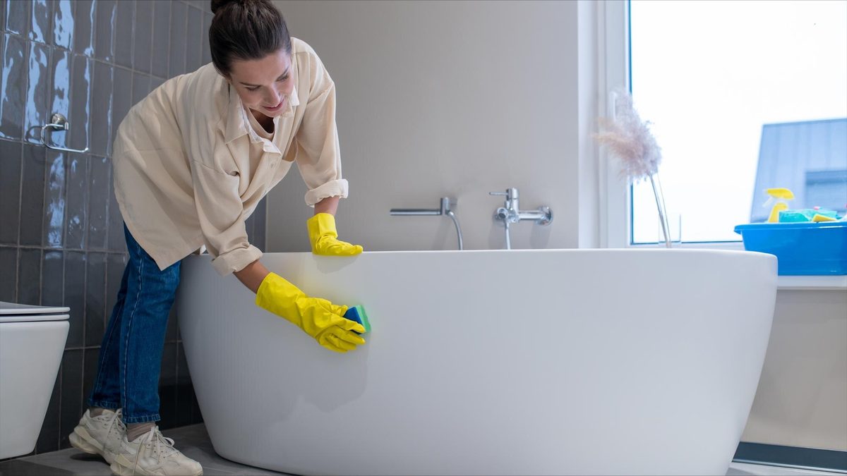 Woman scrubbing bathtub with sponge