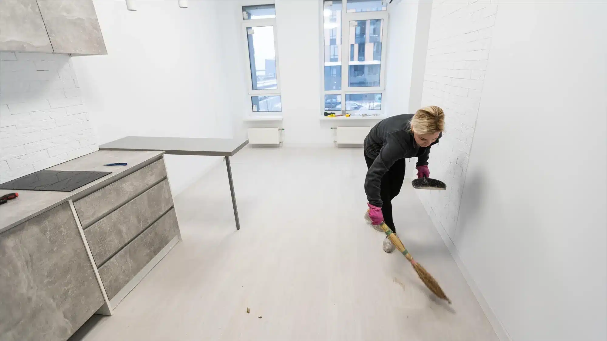 woman sweeping empty apartment floor after renovation