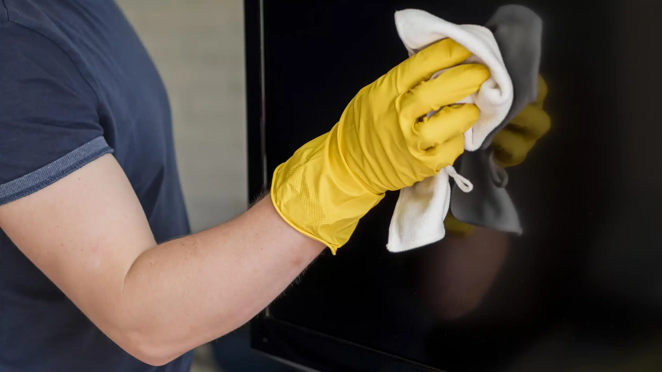 Gloved hand wiping a flat screen TV with a white cloth