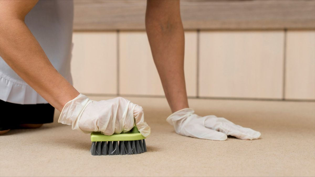 Hands scrubbing floor with brush and gloves