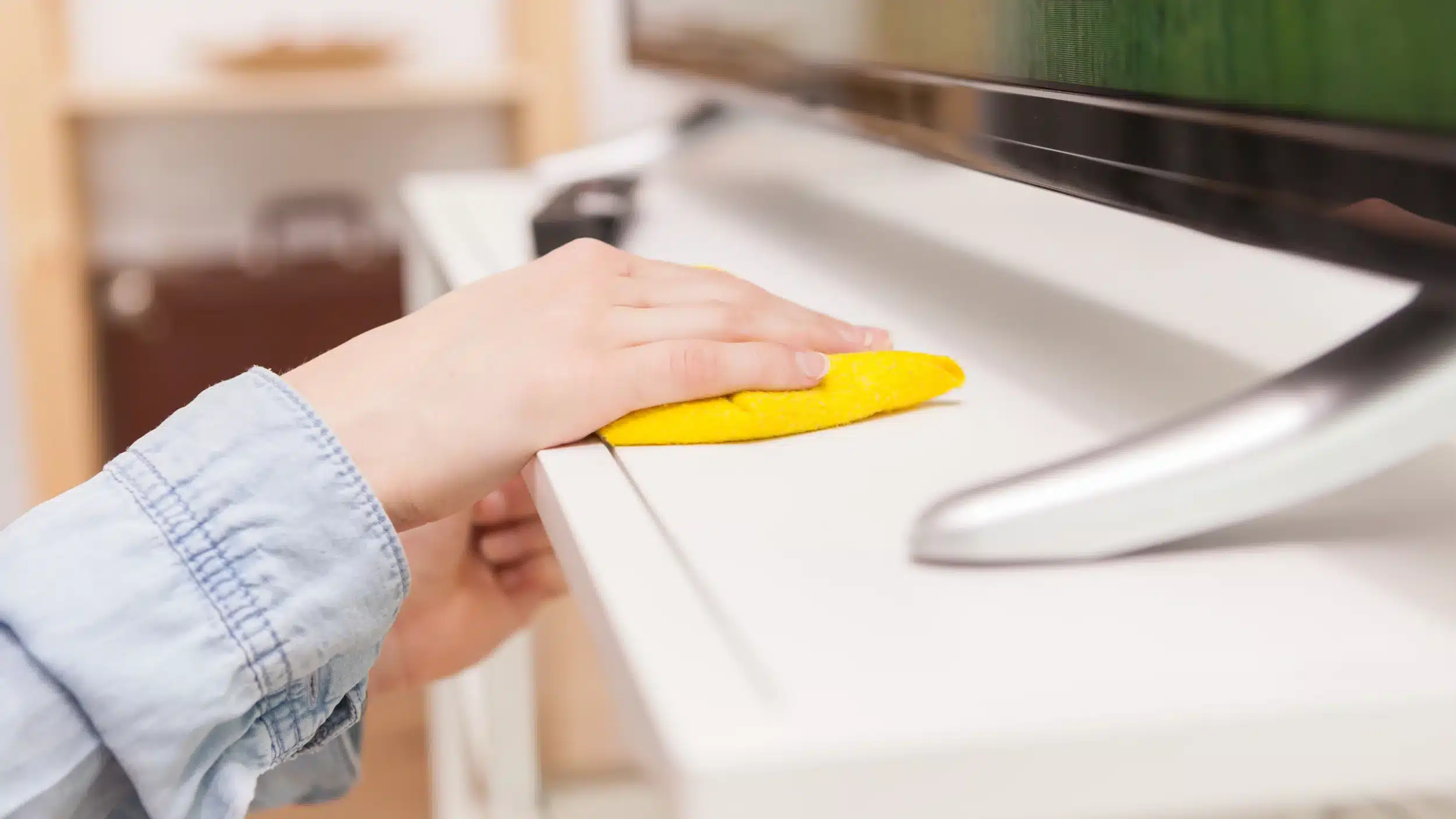 Hand wiping a white TV stand with a yellow microfiber cloth