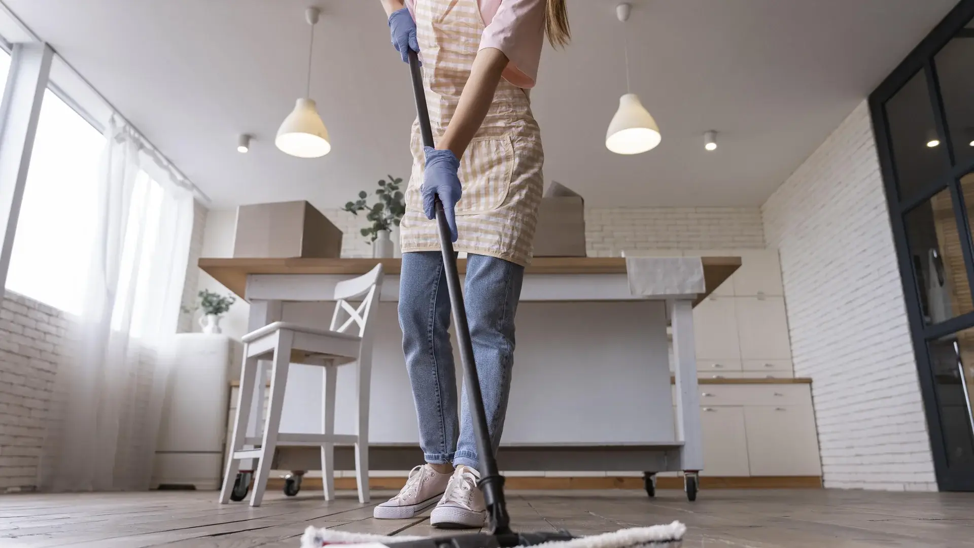 Woman mopping hardwood floor wearing apron and blue gloves