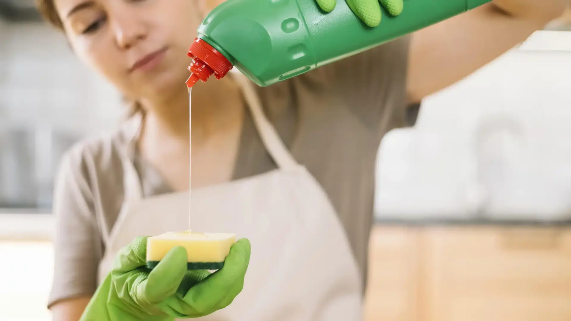 Woman in green gloves pouring dish soap onto a sponge