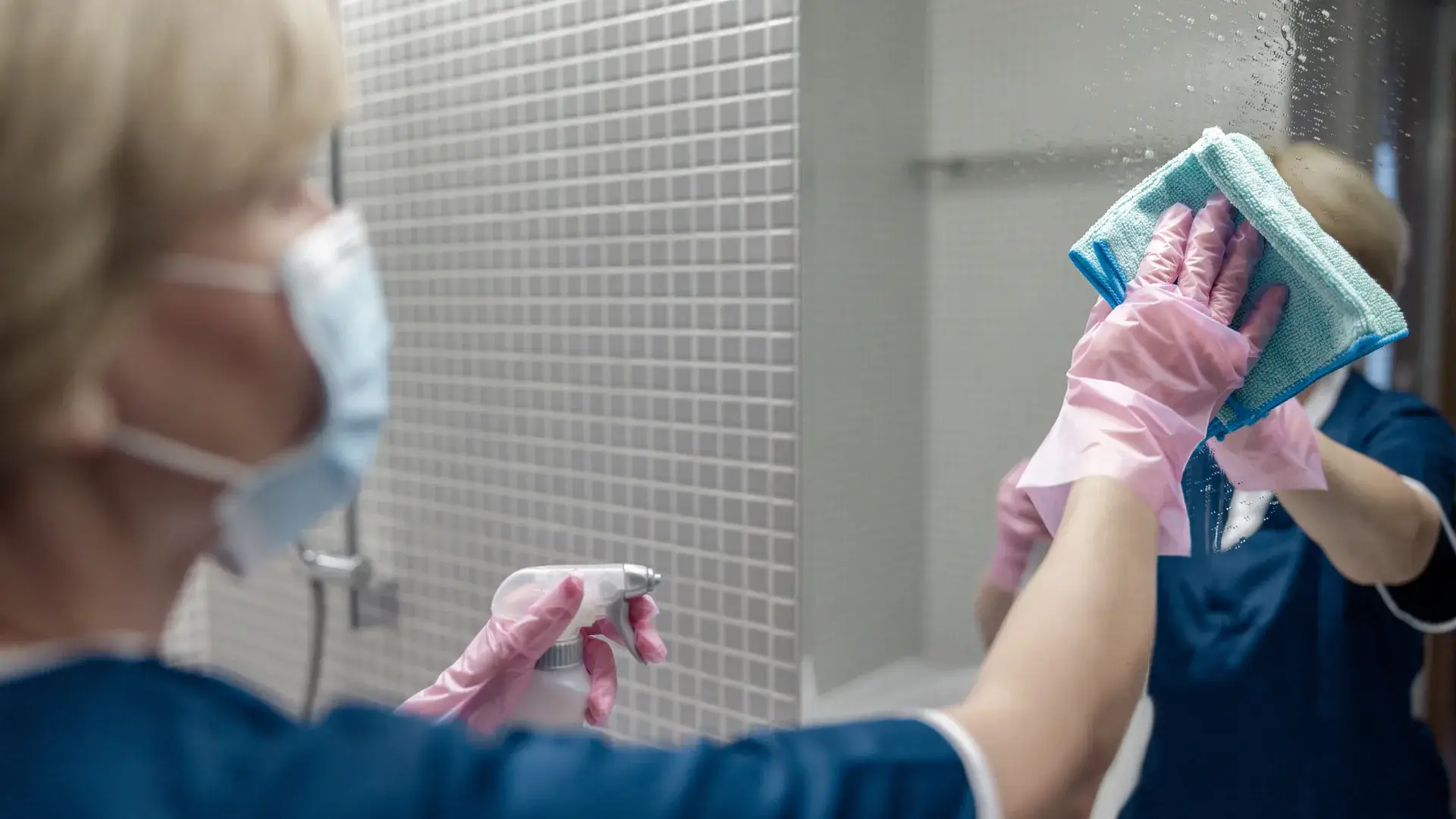 Housekeeper spraying and wiping a bathroom mirror