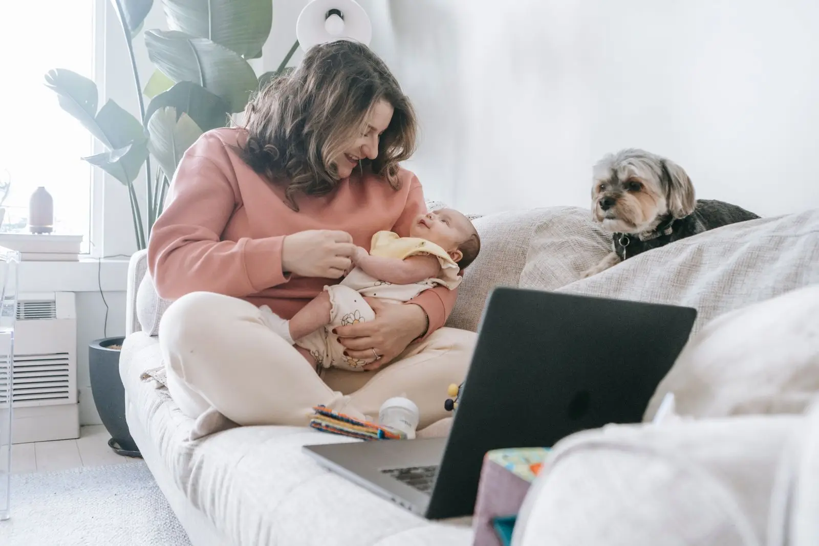 Mother holding a baby on a couch beside the family dog in a bright living room in Aubrey, Texas