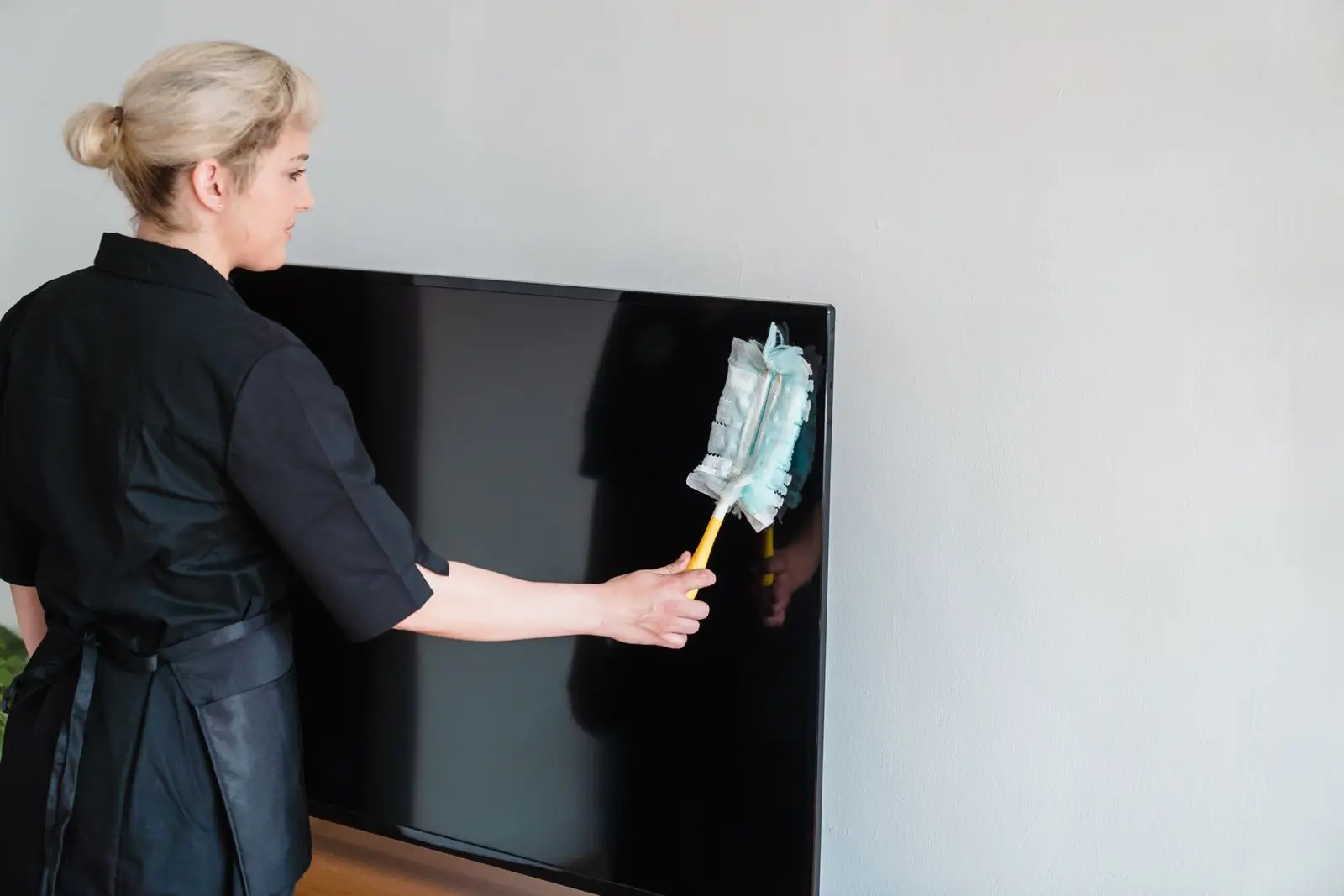 Professional house cleaner dusting a bright living room during a first cleaning visit in McKinney, Texas